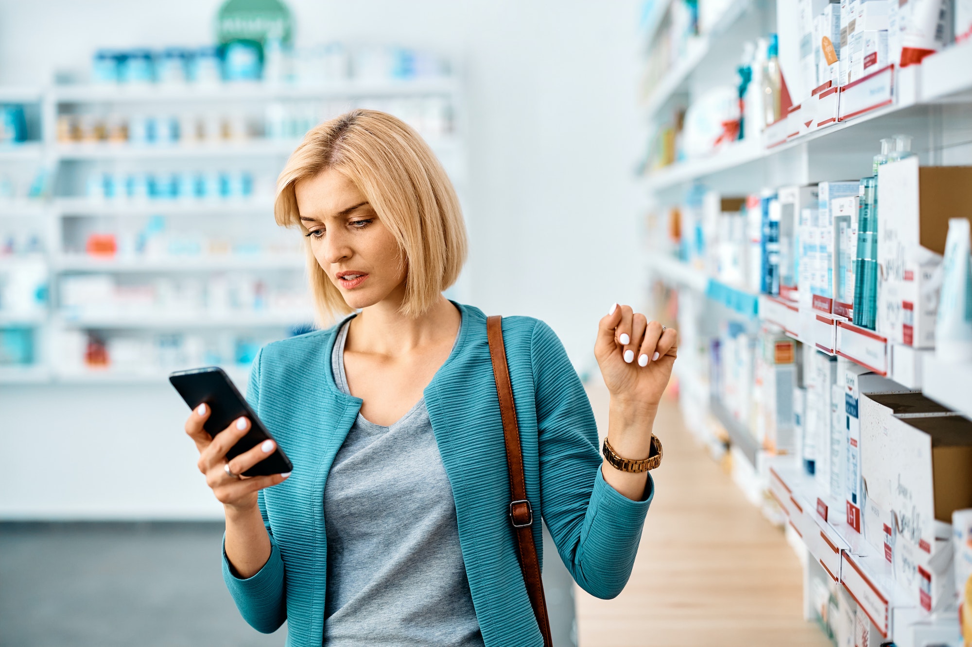 Mid adult woman using mobile phone while buying in pharmacy.
